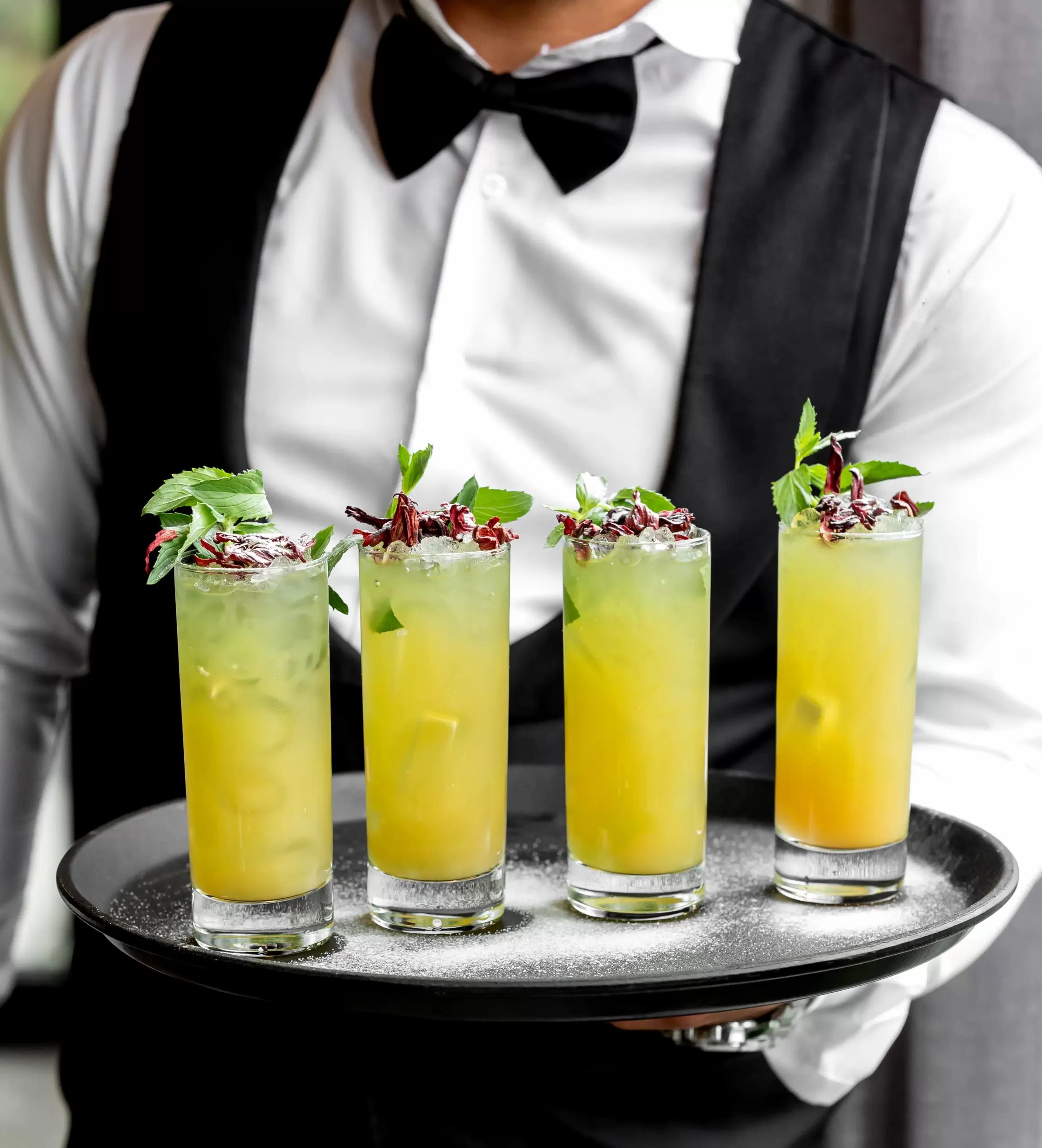 waiter holding tray with lemon mojitos glasses garnished with mint dried roses scaled